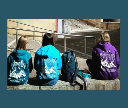 Three people sitting on a wall wearing hoodies in different colours with the HCYO logo on it